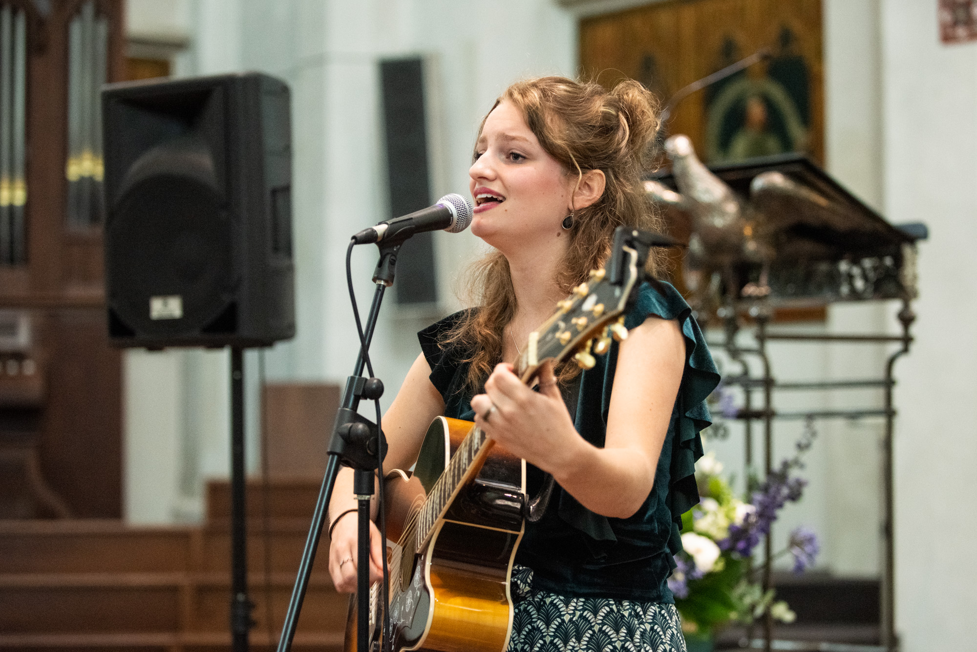 Zangeres met gitaar treedt op in een kerkinterieur